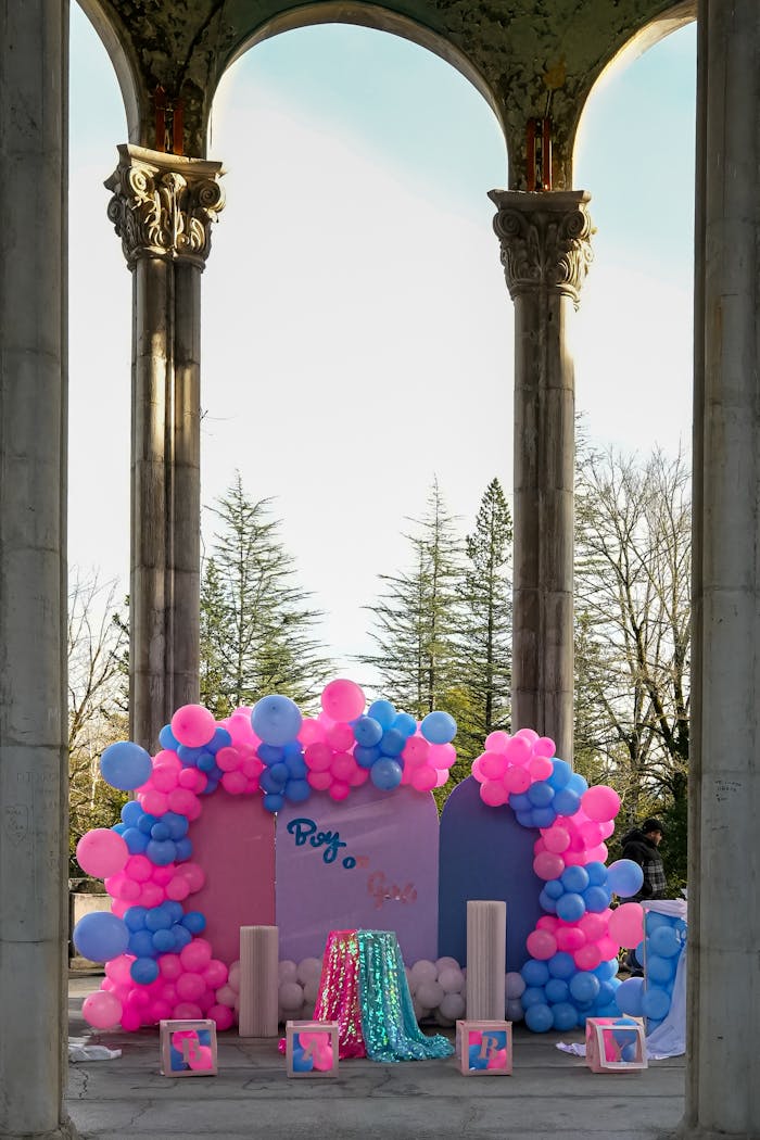 Vibrant gender reveal setup with balloons in blue and pink under a historic pavilion in Kutaisi, Georgia.