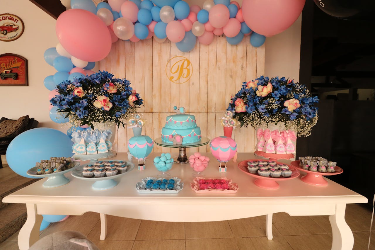 services-04 Vibrant dessert table decorated with blue and pink balloons, flowers, and sweets for a baby shower.